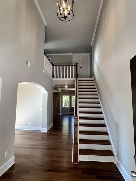 unfurnished dining area with dark wood-type flooring, crown molding, and a notable chandelier