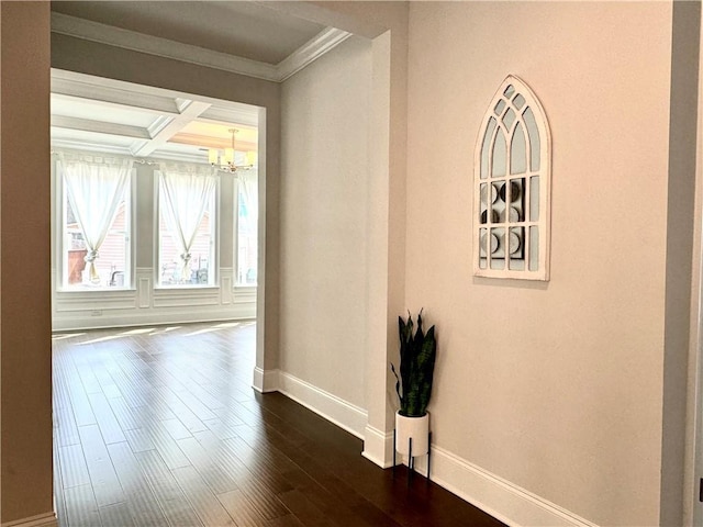 empty room with dark wood finished floors, ornamental molding, a chandelier, coffered ceiling, and baseboards