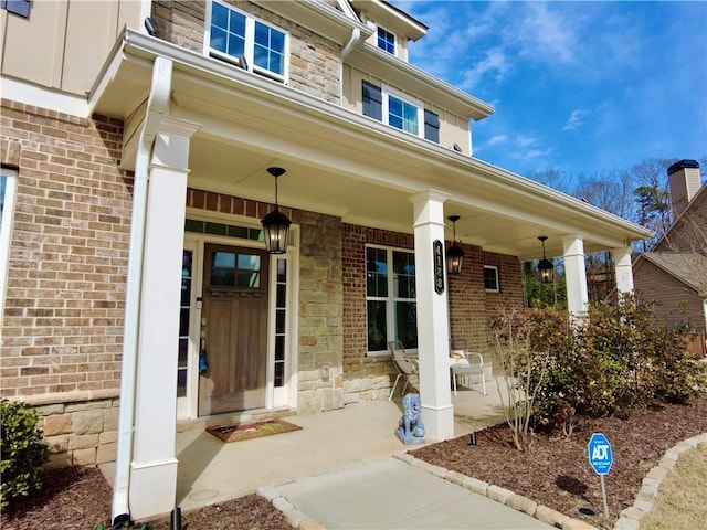 entrance to property with stone siding, brick siding, and a porch