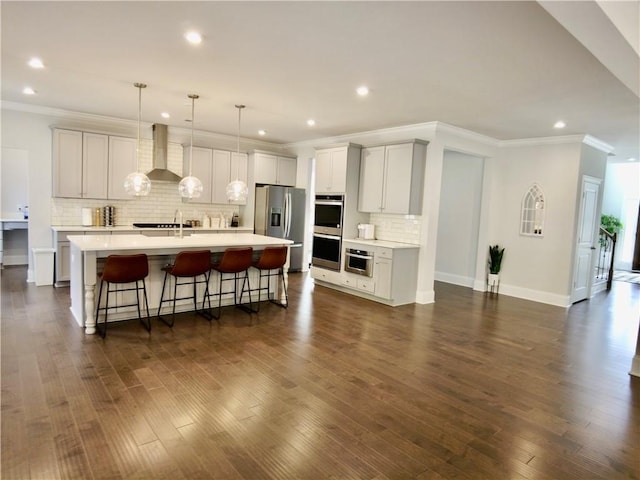 kitchen with wall chimney range hood, light countertops, appliances with stainless steel finishes, a breakfast bar, and dark wood-style floors