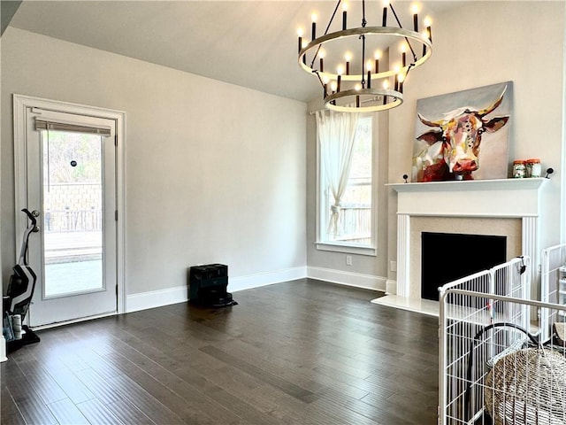 living area with dark wood-style flooring, a wealth of natural light, a notable chandelier, and baseboards