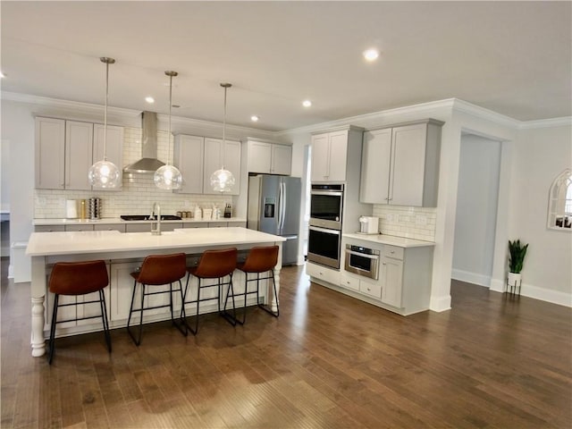 kitchen featuring wall chimney range hood, light countertops, a kitchen island with sink, a kitchen bar, and stainless steel appliances