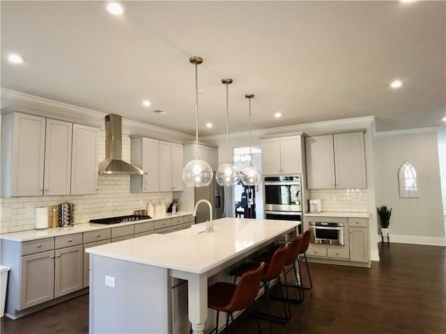 kitchen with wall chimney exhaust hood, double oven, a breakfast bar, cooktop, and gray cabinetry
