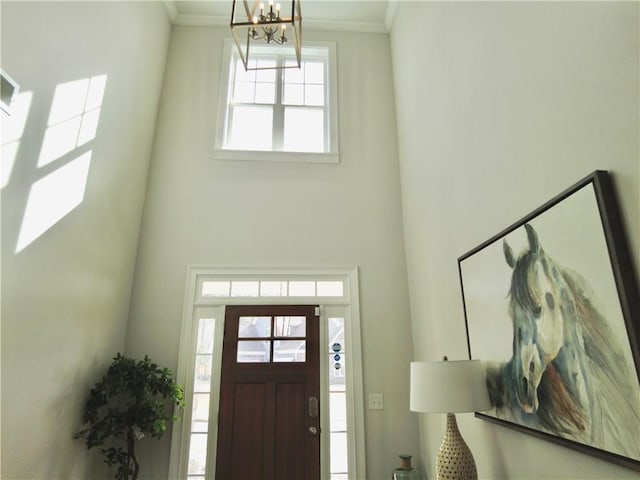 entryway featuring a towering ceiling, an inviting chandelier, and ornamental molding