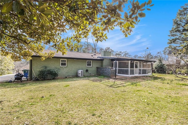 rear view of house with brick siding, a sunroom, a chimney, fence private yard, and a lawn