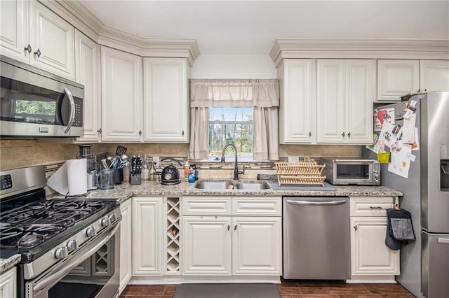 kitchen with light stone countertops, a toaster, appliances with stainless steel finishes, white cabinets, and a sink