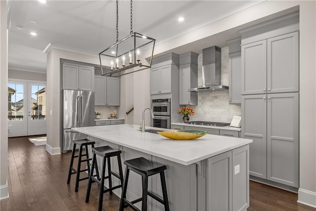 kitchen with wall chimney range hood, stainless steel appliances, a kitchen island with sink, and gray cabinets