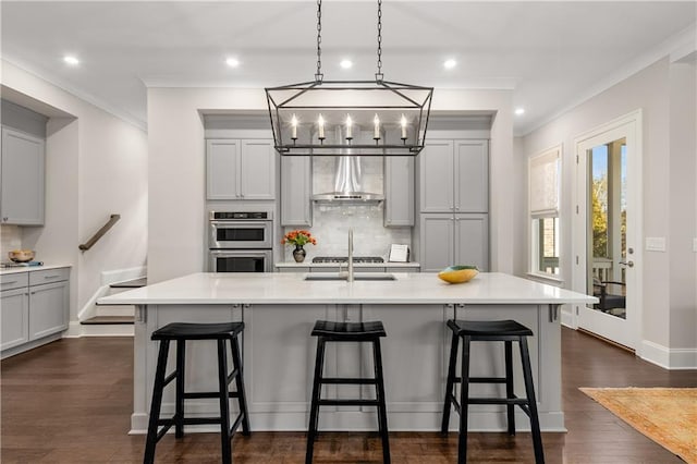 kitchen with a kitchen island with sink, wall chimney exhaust hood, tasteful backsplash, and a kitchen breakfast bar