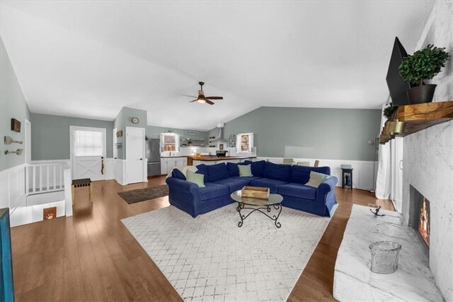 9430 Chestatee Ct, Gainesville, GA 30506 - living room featuring wainscoting, lofted ceiling, wood finished floors, ceiling fan, and a lit fireplace