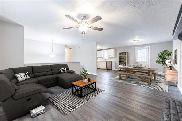 living room with visible vents, a ceiling fan, a textured ceiling, baseboards, and dark wood-style flooring