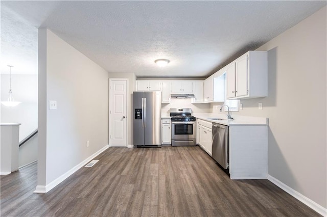 kitchen with under cabinet range hood, appliances with stainless steel finishes, dark wood-style floors, white cabinets, and a sink