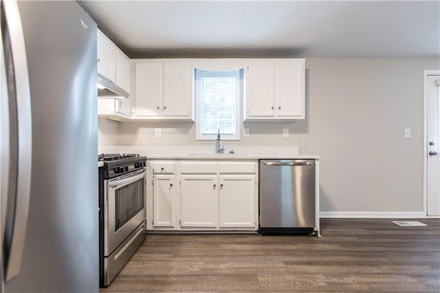 kitchen with under cabinet range hood, dark wood finished floors, appliances with stainless steel finishes, white cabinets, and a sink