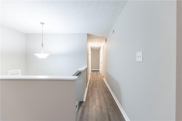 hall featuring an upstairs landing, a textured ceiling, wood finished floors, baseboards, and attic access