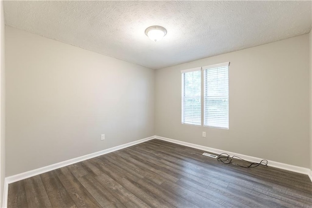 spare room with dark wood finished floors, visible vents, a textured ceiling, and baseboards