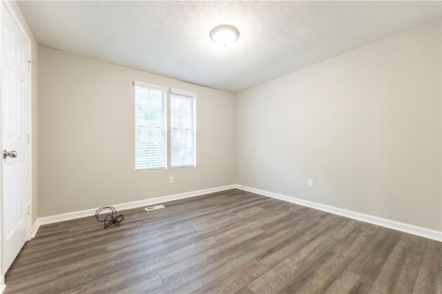 spare room with visible vents, baseboards, a textured ceiling, and dark wood-style floors