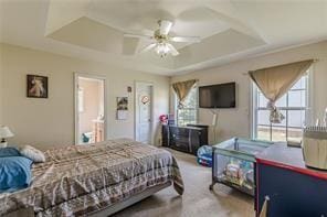 bedroom featuring ensuite bathroom, carpet, ceiling fan, and a tray ceiling