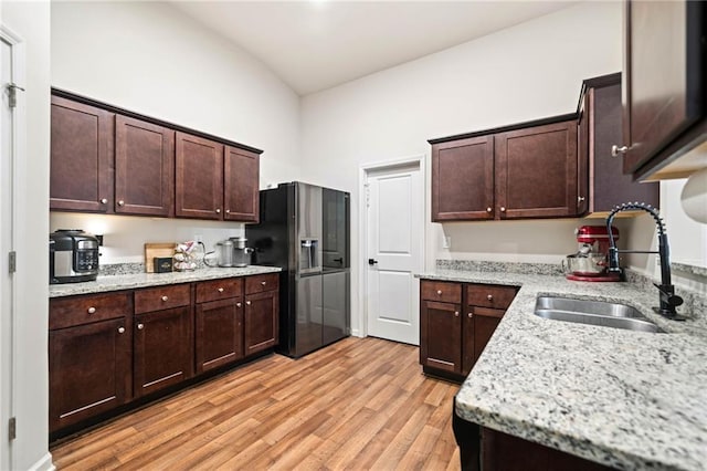 kitchen with dark brown cabinetry, light wood-style flooring, light stone countertops, fridge with ice dispenser, and a sink