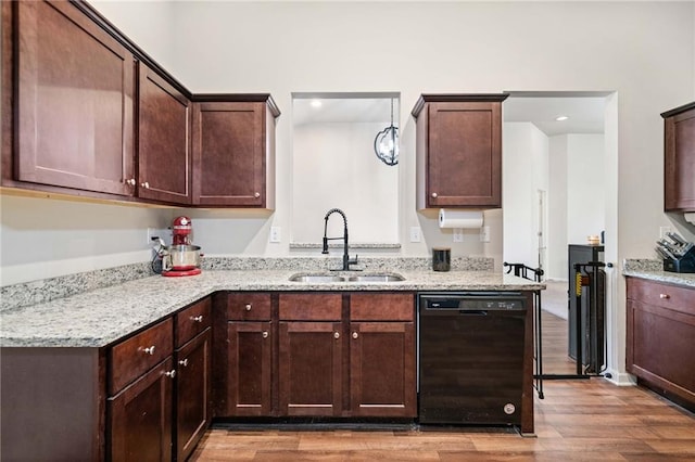 kitchen with dark brown cabinetry, black dishwasher, light stone counters, wood finished floors, and a sink