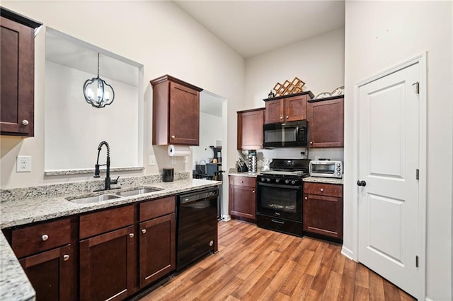 kitchen featuring black appliances, light wood finished floors, a sink, and light stone countertops