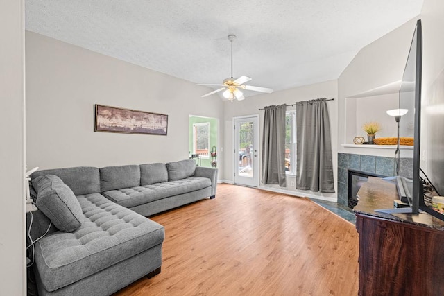 living room featuring lofted ceiling, a textured ceiling, wood finished floors, and a tile fireplace