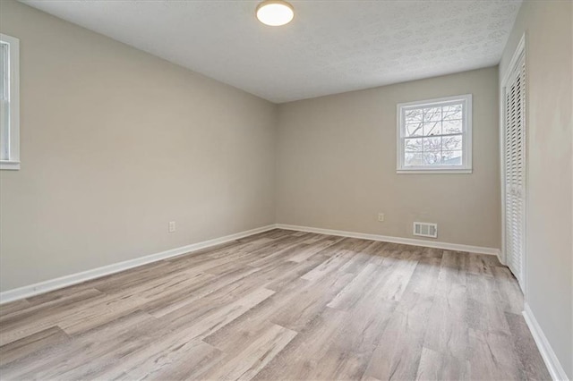 unfurnished room with baseboards, visible vents, light wood-style flooring, and a textured ceiling