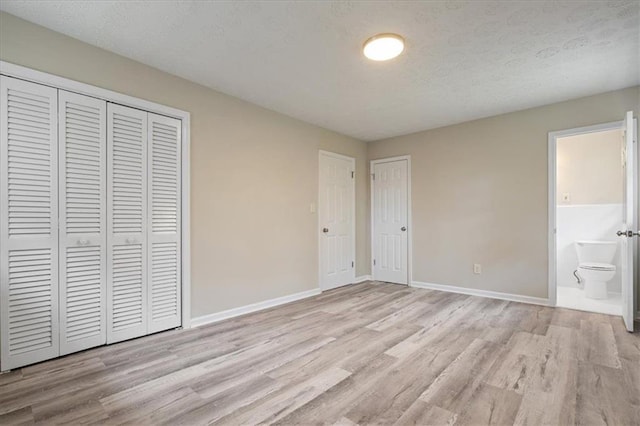 unfurnished bedroom with connected bathroom, baseboards, light wood-style floors, and a textured ceiling