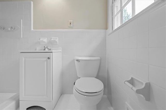 bathroom with toilet, vanity, a wainscoted wall, and tile walls