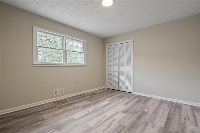 unfurnished bedroom with baseboards, a textured ceiling, visible vents, a closet, and wood finished floors