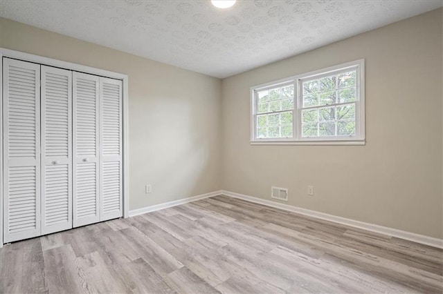 unfurnished bedroom with a closet, a textured ceiling, light wood-type flooring, baseboards, and visible vents