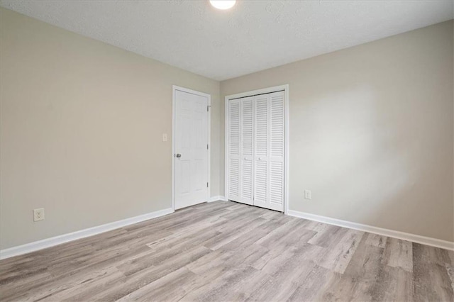 unfurnished bedroom with baseboards, a textured ceiling, a closet, and light wood-type flooring