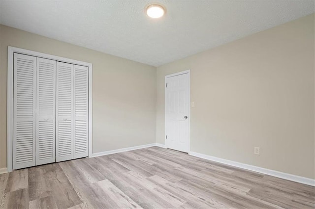 unfurnished bedroom with baseboards, a textured ceiling, wood finished floors, and a closet