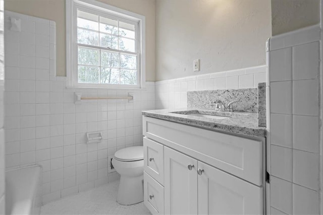 full bath with vanity, tile walls, toilet, a bathtub, and wainscoting