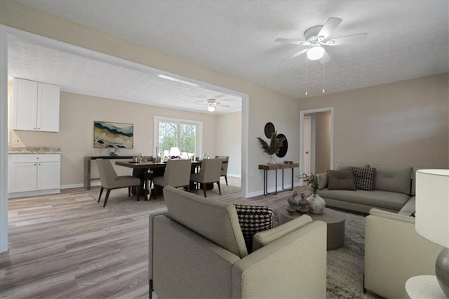 living room with baseboards, a textured ceiling, ceiling fan, and light wood finished floors