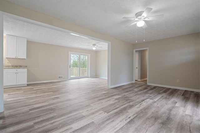 unfurnished living room featuring a textured ceiling, light wood-style floors, baseboards, and a ceiling fan