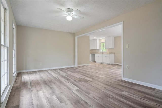 unfurnished living room featuring a ceiling fan, baseboards, light wood finished floors, and a textured ceiling