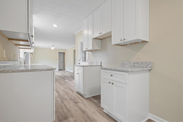 kitchen with light wood finished floors, white cabinets, light stone countertops, and a textured ceiling