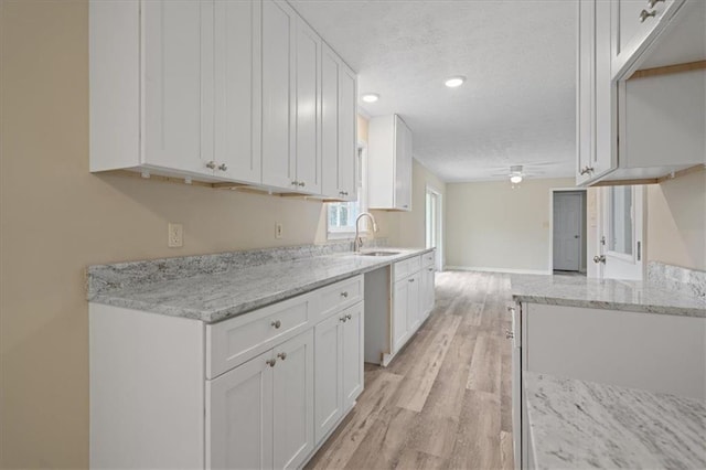 kitchen featuring a textured ceiling, a sink, ceiling fan, and white cabinets