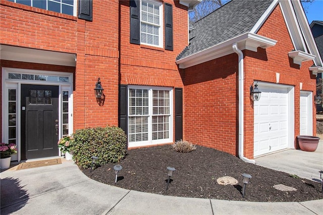 property entrance with a garage, brick siding, and roof with shingles