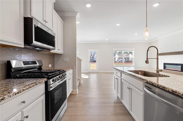 kitchen with sink, hanging light fixtures, stainless steel appliances, light hardwood / wood-style floors, and a kitchen island with sink