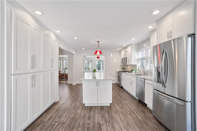 kitchen with stainless steel appliances, dark wood-type flooring, white cabinetry, a sink, and a kitchen island