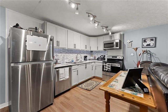 kitchen featuring light wood finished floors, appliances with stainless steel finishes, a sink, light countertops, and backsplash