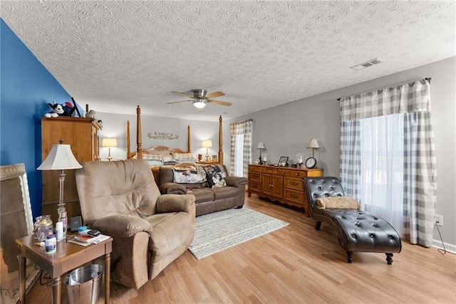 living area with a textured ceiling, a ceiling fan, visible vents, and light wood-style floors