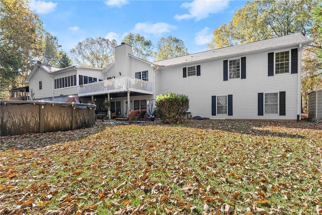 back of property featuring a sunroom, a covered pool, a chimney, and a deck