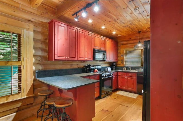 kitchen with sink, a kitchen bar, hanging light fixtures, black appliances, and light wood-type flooring