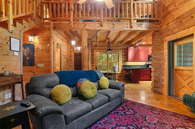 living room with rustic walls, light hardwood / wood-style flooring, wooden ceiling, ceiling fan, and beam ceiling