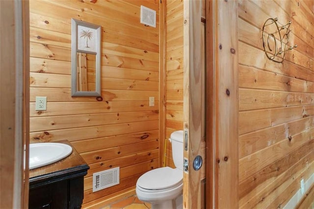 bathroom featuring vanity, toilet, tile patterned flooring, and wood walls