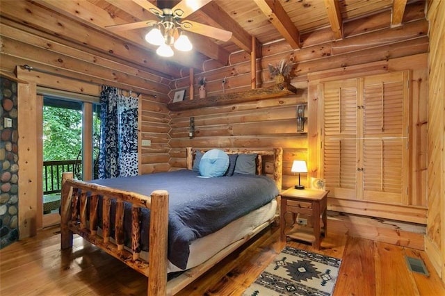 bedroom featuring access to exterior, beamed ceiling, hardwood / wood-style flooring, ceiling fan, and log walls