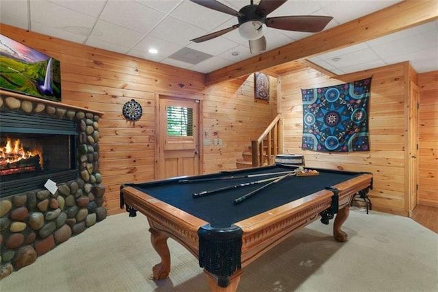 recreation room with a stone fireplace, carpet floors, ceiling fan, and wood walls