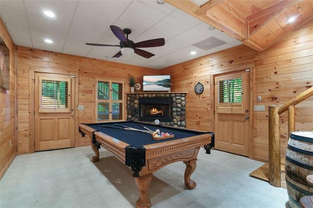 recreation room with a stone fireplace, pool table, carpet flooring, wooden walls, and ceiling fan