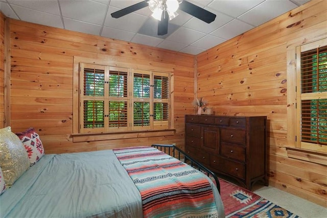 carpeted bedroom with ceiling fan, a drop ceiling, and wood walls